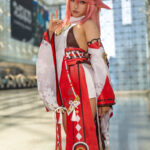 Yae Miko cosplay by @notchasiu from Genshin Impact at Anime NYC 2025 Javits Center, featuring pink hair, fox ears, red and white shrine maiden outfit with floral sleeves and gold tassels – animenyc.com.