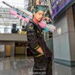 Cyberpunk cosplay by @notthatguyleon at Anime NYC 2025 Javits Center, featuring teal hair, black futuristic jacket with neon details, and massive pastel neon weapon over shoulder – animenyc.com.
