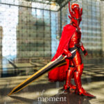 Solo Leveling crimson knight cosplay by @sirjuliuscosplay at Anime NYC 2025 Javits Center, featuring full red armor, horned helmet, flowing cape, golden sword, and dramatic mirrored aura effect – animenyc.com.