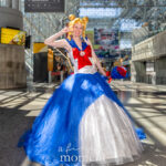Sailor Moon princess gown cosplay by @chibimaicosplay at Anime NYC 2025 Javits Center, featuring blue and white ball gown with red bow, golden odango hairstyle, and bouquet of roses – animenyc.com.