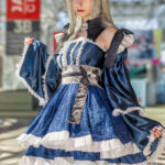 Mutsumi Wakaba cosplay by @2.5dangel at Anime NYC 2025 Javits Center, featuring layered blue brocade dress with white ruffles, silver wig, bow headpiece, and red garters – animenyc.com.