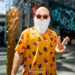 @sir_liamthelegend cosplaying Master Roshi from Dragon Ball with orange Hawaiian shirt, white beard, sunglasses, and staff at Anime NYC 2025 Javits Center – animenyc.com.