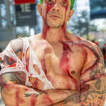 @dannycarmelo cosplaying a battle-damaged Roronoa Zoro from One Piece with green hair, blood-stained body, torn shirt, and katanas at Anime NYC 2025 inside Javits Center – animenyc.com.