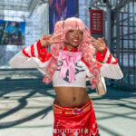 @alliexd3 cosplaying Perona from One Piece with pink curly wig, red and white outfit, and peace sign pose at Anime NYC 2025 Javits Center – animenyc.com.