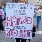 A protester displays a handmade sign reading “YOU CAN’T SPELL HATRED WITHOUT RED HAT” during the No Kings March in New York City on October 18, 2025, connecting political symbolism to messages of intolerance.