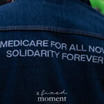 A person wearing a denim jacket with white embroidered text reading “MEDICARE FOR ALL NOW, SOLIDARITY FOREVER” during the ICE OUT of NYC protest in Manhattan on October 22, 2025.