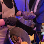 Close-up of a caterer shucking oysters at the CHiPS Annual Gala 2025 in Park Slope, Brooklyn, with a bucket of oysters and lemons under warm purple lighting.