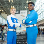 Cosplayers @Matthew_dion20 and @justincosplays dressed as members of the Fantastic Four pose with arms crossed in front of a New York Comic Con sign inside the Javits Center.