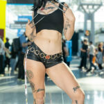 Cosplayer @heyitsmxdz dressed as X-23 from X-Men poses with extended claws at New York Comic Con 2025, wearing a black crop top, leather shorts, chain belt with X-Men emblem, and knee-high boots.