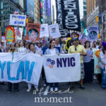 A large group of protesters in Times Square holds banners reading “FREE DYLAN,” “NYIC,” and “El Puente: Leaders for Peace & Justice” during the No Kings March in New York City on October 18, 2025.