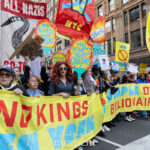 A large group of protesters holds bright yellow banners and colorful signs reading “NO KINGS JUST QUEENS” and “PEOPLE OVER BILLIONAIRES” during the No Kings March in New York City on October 18, 2025.