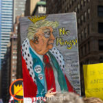 A hand-painted protest sign depicts Donald Trump wearing a golden crown and royal robe with the words “No Kings!” held high during the No Kings March in New York City on October 18, 2025.