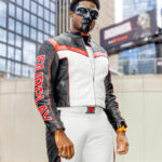 Cosplayer @justincosplays dressed as Mister Terrific from DC Comics at New York Comic Con 2025, wearing a black and white leather suit with red accents and “FAIR PLAY” on the sleeve, posing outside the Javits Center in NYC.