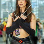 Cosplayer @onyourleftsam dressed as X-23 from Marvel’s X-Men at New York Comic Con 2025, crossing her arms to display metal claws, wearing black leather pants, a cropped top, and an X-Men belt inside the Javits Center in NYC.