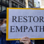 A protester wearing a mask and black beanie holds a sign that reads “Restore Empathy” during the No Kings March in New York City on October 18, 2025.