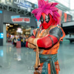 Cosplayer @maverick_warner dressed as a Super Saiyan version of Deadpool at New York Comic Con 2025, wearing a pink spiky wig and a battle-damaged orange and blue gi inside the Javits Center in NYC.
