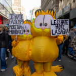 Two people in inflatable Garfield costumes hold protest signs that read “I Hate Fascism More Than Mondays” and “Less Hate More Lasagna” during the No Kings March in New York City.