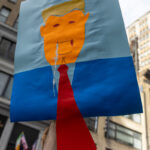 A protester holds up a handmade caricature sign of Donald Trump with a red tie during the No Kings March in New York City.