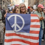 A woman holds a modified American flag with a blue peace sign replacing the stars during the No Kings March in New York City.