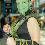 Cosplayer @sweettee816 dressed as Reptile from Mortal Kombat at New York Comic Con 2025, wearing a green quilted vest with the Mortal Kombat insignia and detailed reptilian makeup at the Javits Center in NYC.