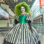 Cosplayer @queenycece181 dressed as Beetlejuice at New York Comic Con 2025, wearing a black-and-white striped ball gown with green corset, moss, and bug details inside the Javits Center in NYC.