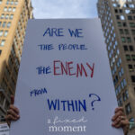 Protester holds a white sign that reads “Are we the people the enemy from within?” written in blue and red letters during the No Kings March in New York City.
