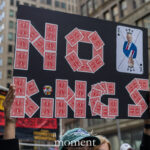 Protester holds a black poster made of red playing cards spelling “NO KINGS,” with a King of Spades card depicting Donald Trump at the top right, during the No Kings March in New York City.