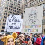 Protesters at the No Kings March hold signs reading “Fight Ignorance Not Immigrants” and “I Want You in Prison” with a hand-drawn Uncle Sam illustration in New York City.