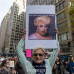 Protester at the No Kings March in New York City holds a sign showing a drag queen with the caption “New Drag Name: ReLisa D’Files.”
