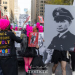 Protesters wearing pink balaclavas and carrying anti-fascist signs march through Manhattan during the No Kings March, including a large image of an authoritarian figure in a Nazi uniform and a jacket reading “TRUE AMERICANS REVOLT AGAINST KINGS.”