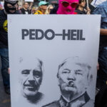 Protester in a bright pink mask and sunglasses holds a large sign reading “PEDO-HEIL” with edited black-and-white portraits of Donald Trump and Jeffrey Epstein at the No Kings March in New York City.