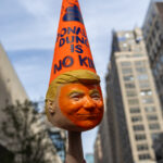 A protester raises a handmade orange Trump head sculpture topped with a cone-shaped dunce cap reading “DONALD DUNC IS NO KING” during the No Kings March in New York City.