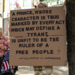 Protester holds a large cardboard sign quoting the Declaration of Independence during the No Kings March in New York City, reading “A prince, whose character is thus marked by every act which may define a tyrant, is unfit to be the ruler of a free people.”