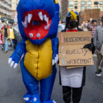 Protesters in dinosaur and penguin costumes march holding a sign that reads “Indiscriminate Cruelty Enforcement” during the No Kings March in New York City.