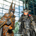 Cosplayers @critical.mask and @steampunkdbatmanvol2 dressed as The Batman Who Laughs and Steampunk Batman pose together in detailed armor inside the Javits Center at New York Comic Con 2025.