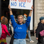 Smiling protester wearing a blue “Yalla” sweatshirt holding a sign that reads “No Kings, No Cuomo, No ICE” during the No Kings March in New York City.