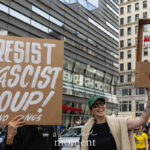 Protesters at the No Kings March in NYC hold a cardboard sign reading “Resist the Fascist Coup! No Kings” and a handmade guillotine prop with “No Kings” written in red paint.