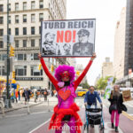 Protester in a pink and red costume with a heart reading “LOVE WINS” holds a sign that says “TURD REICH NO!” with images of Donald Trump and Nazi officers at the No Kings March in New York City.
