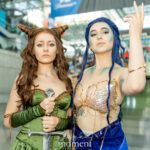 Cosplayers @gennareading and @kiragodley dressed as Jude Duarte and Nicasia from The Cruel Prince pose together at the Javits Center during New York Comic Con 2025 — one in a green gown holding a sword, the other in a blue and gold sea-inspired costume.