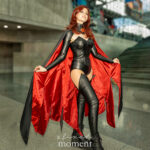 Cosplayer @miss_magitek as Madelyne Pryor, the Goblin Queen from X-Men, wearing a black leather bodysuit, thigh-high boots, and a black cape with a red satin lining, standing confidently at New York Comic Con 2025 inside the Javits Center.