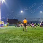 A soccer player in a purple jersey takes a penalty kick as the goalkeeper braces to defend, during “The Cost of Living Classic” soccer tournament at Maimonides Park in Coney Island at dusk.