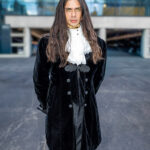 Cosplayer @mpny dressed as Louis de Pointe du Lac from Interview with the Vampire, wearing a black velvet coat with lace cravat and standing in front of the Javits Center glass façade at New York Comic Con 2025.