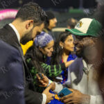 Zohran Mamdani shakes hands and smiles with a supporter wearing a green hat after “The Cost of Living Classic” soccer tournament at Maimonides Park in Coney Island.