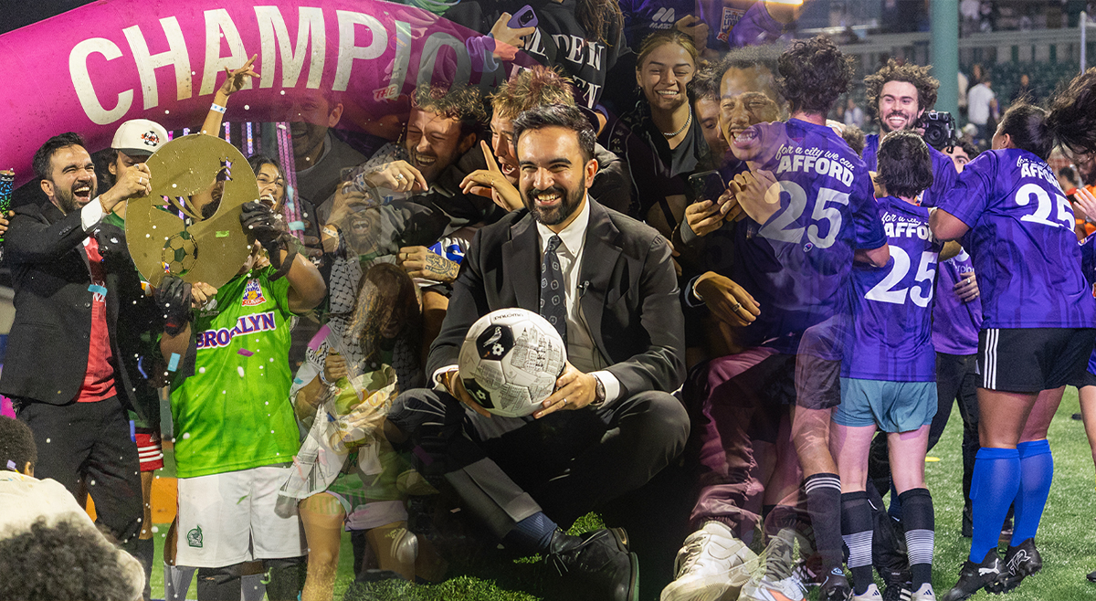 Zohran Mamdani sits smiling with a soccer ball surrounded by cheering players and supporters wearing purple and green jerseys at Maimonides Park in Coney Island, under a bright pink “CHAMPIONS” arch during The Cost of Living Classic tournament on October 19, 2025.