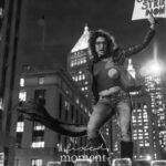 A person in a leather jacket and jeans stands on a barricade holding a sign that says “STRIKE NOW” during the ICE OUT of NYC protest in Manhattan on October 22, 2025.