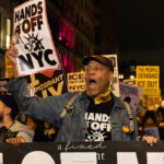Activist @jaywwalker holds a “HANDS OFF NYC” sign while leading chants at night during the ICE OUT of NYC protest in Manhattan on October 22, 2025.