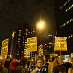 A large crowd marches through Lower Manhattan at night holding yellow protest signs that read “THE PEOPLE DEMAND ICE OUT OF OUR COMMUNITIES!” during the ICE OUT of NYC protest on October 22, 2025.