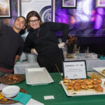 Two people from Runner & Stone posing behind a catering table with plates of sliders at the 2025 CHiPS Annual Gala in Park Slope, Brooklyn.