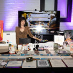 A woman stands behind a silent auction table filled with gift certificates, artwork, and items at the 2025 CHiPS Annual Gala in Park Slope, Brooklyn.