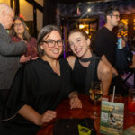 Two women seated at a table smiling at the camera during the CHiPS Annual Gala 2025 in Brooklyn, with drinks and a “Donate to CHiPS” flyer visible on the table.